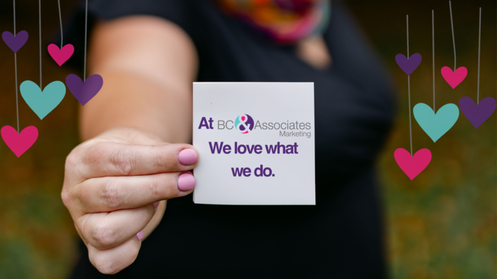Holding a card saying "At BC & Associates Marketing, We love what we do"